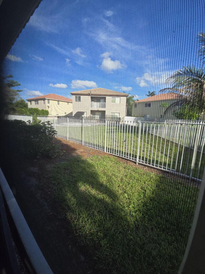 View of a grassy backyard and apartment buildings through a window screen — 6511 Sandy Bank Terrace, Riviera Beach FL 33407, RIVIERA BEACH, FL