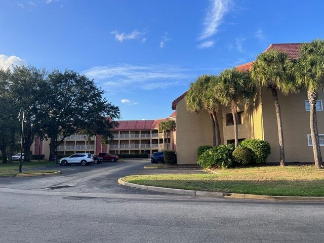 A multi-story apartment building with a red roof stands behind a parking lot and trees — 6337 Parc Corniche Dr Drive # 2111, Orlando FL 32821, ORLANDO, FL