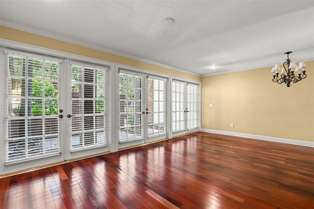 An empty room with hardwood floors, yellow walls, a chandelier, and multiple glass-paned French doors — 1134 WASHINGTON AVENUE UNIT 13C, WINTER PARK, FL