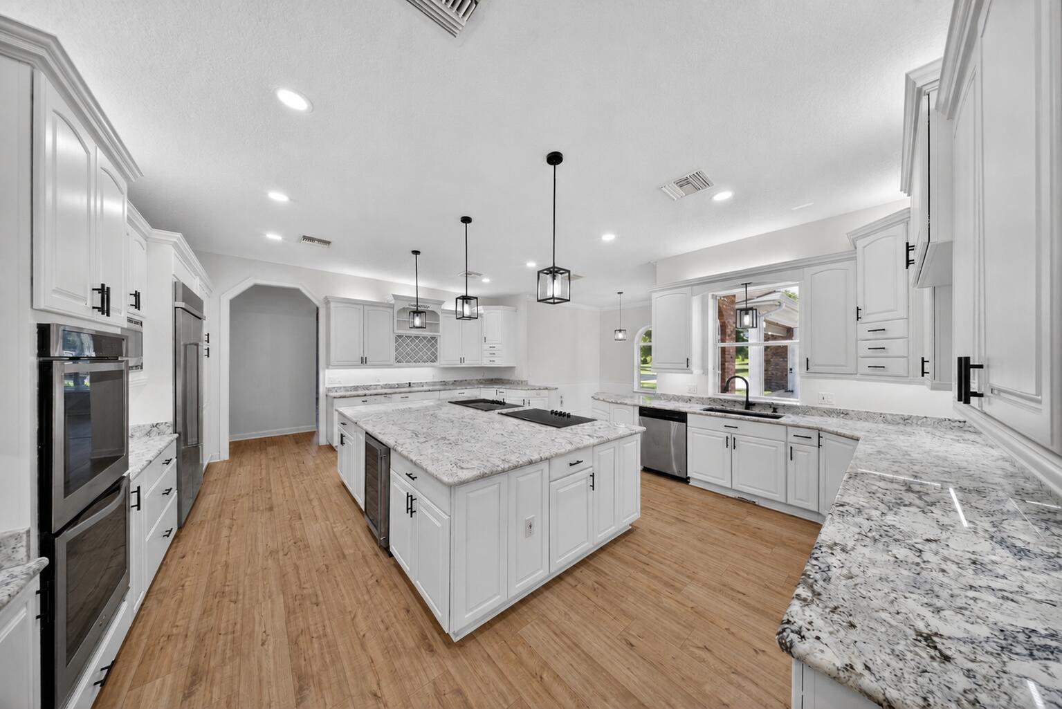 A bright kitchen features white cabinets, granite countertops, a large island, and light wood flooring — 8686 Andrews Avenue, Fort Pierce FL 34945, FORT PIERCE, FL
