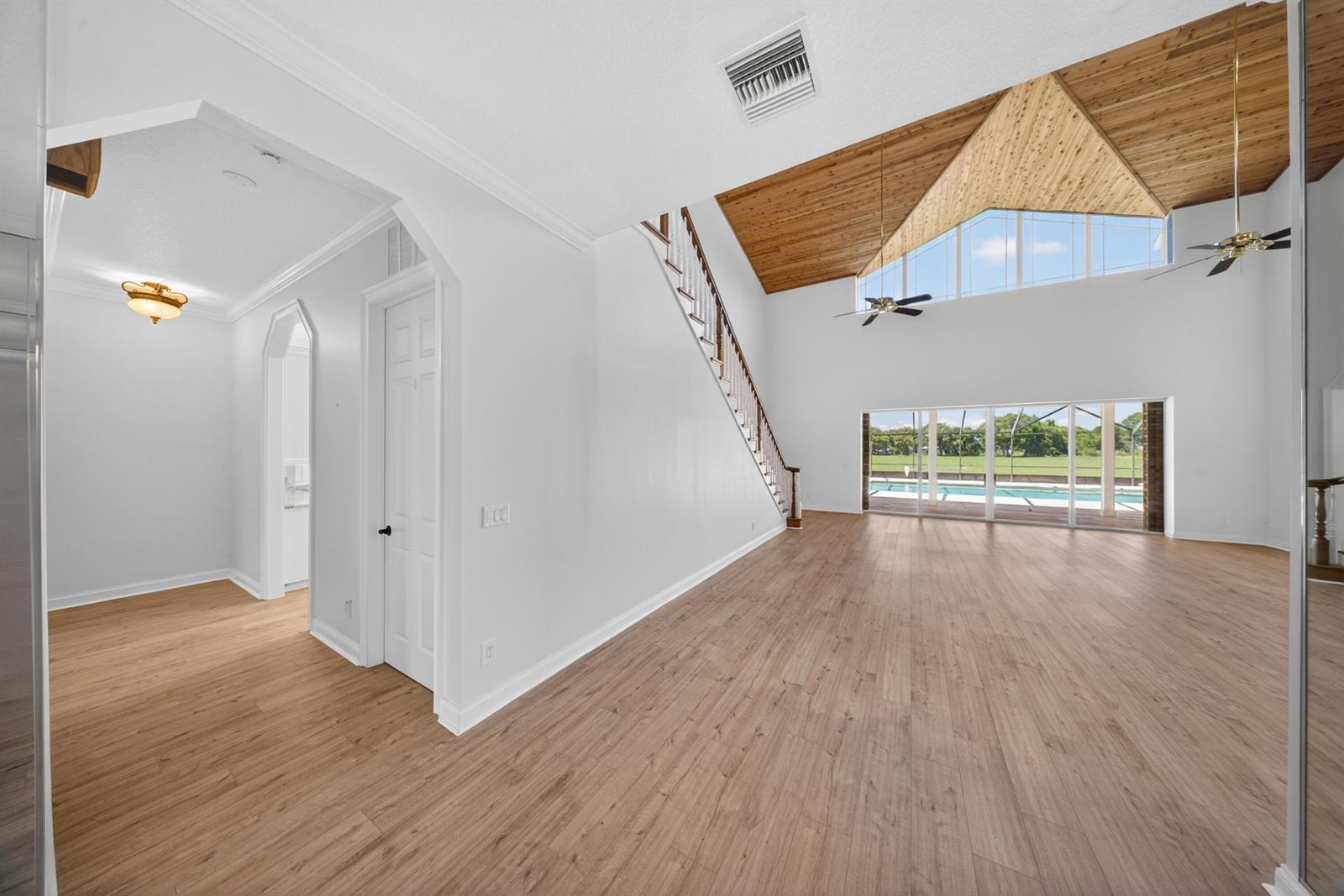 A spacious living room features light wood flooring, a vaulted wood ceiling, and a staircase — 8686 Andrews Avenue, Fort Pierce FL 34945, FORT PIERCE, FL