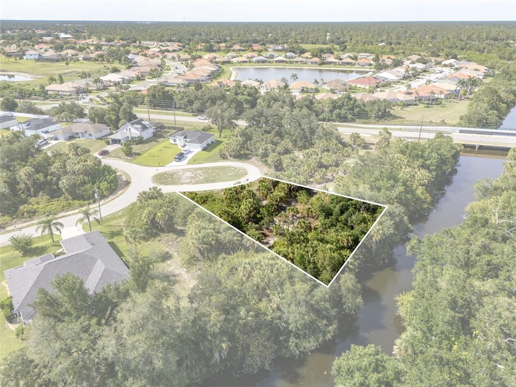 An aerial view shows a vacant, wooded lot bordered by a canal and residential streets — Lot 15 ROANOKE ROAD, NORTH PORT, FL