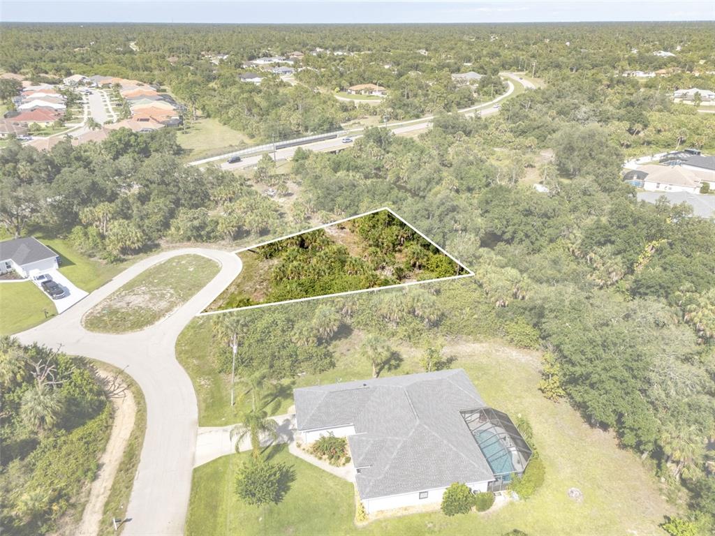 An aerial view shows a vacant, triangular-shaped residential lot next to a house with a pool — Lot 15 ROANOKE ROAD, NORTH PORT, FL