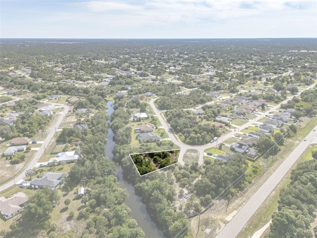 An aerial view shows a vacant, wooded lot bordered by a canal and a road — Lot 15 ROANOKE ROAD, NORTH PORT, FL