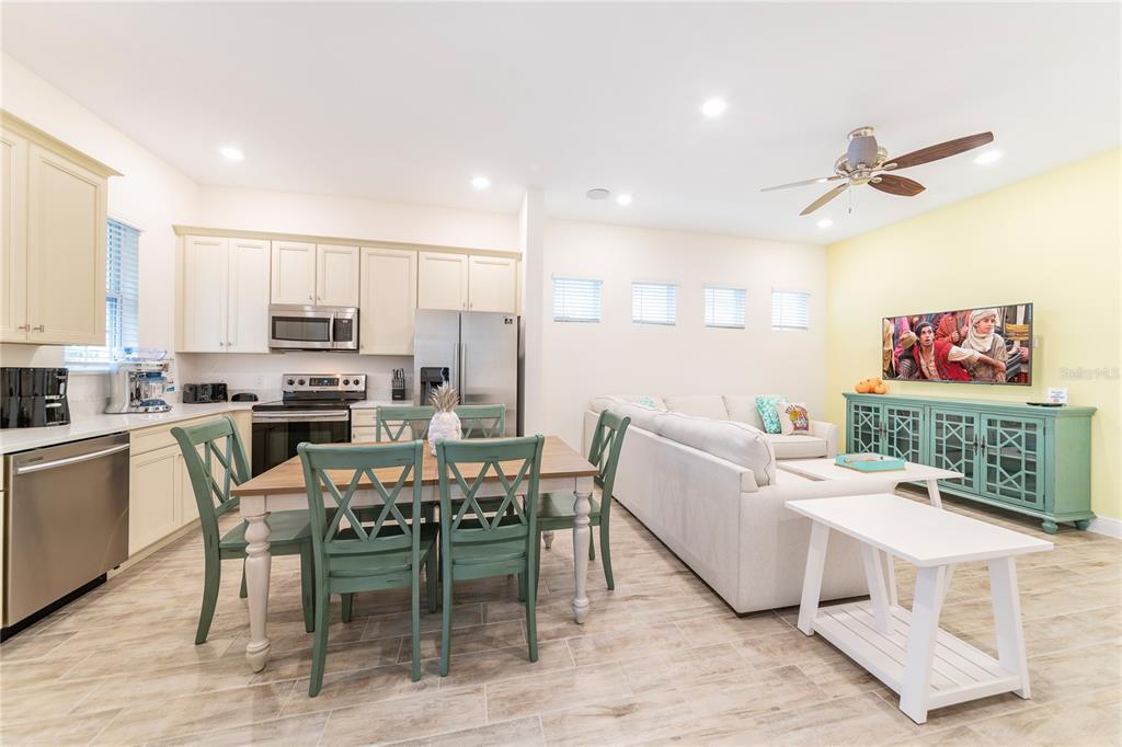 An open-concept kitchen and living area features light cabinetry, teal dining chairs, and tile flooring — 2988 SALTED RIM ROAD, KISSIMMEE, FL