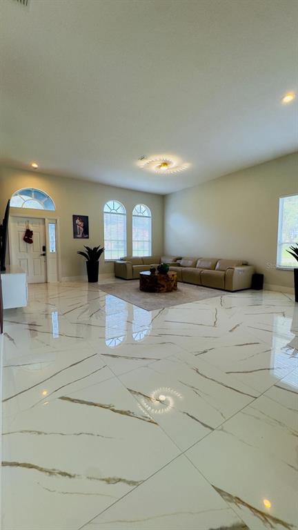 A spacious living room features large white marble-look floor tiles and a beige sectional sofa — 35609 WELBY COURT, ZEPHYRHILLS, FL