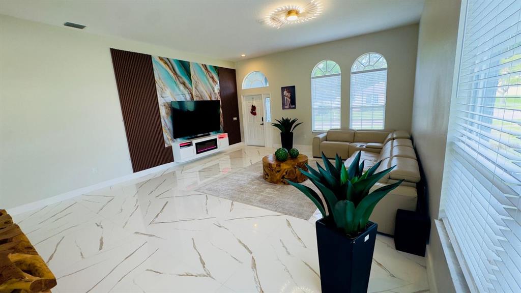 A living room features white marble-look tile floors, a large sectional sofa, and a television — 35609 WELBY COURT, ZEPHYRHILLS, FL
