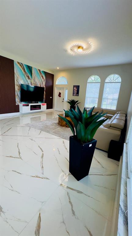 A living room features white marble-look tile floors, a large television, and arched windows — 35609 WELBY COURT, ZEPHYRHILLS, FL