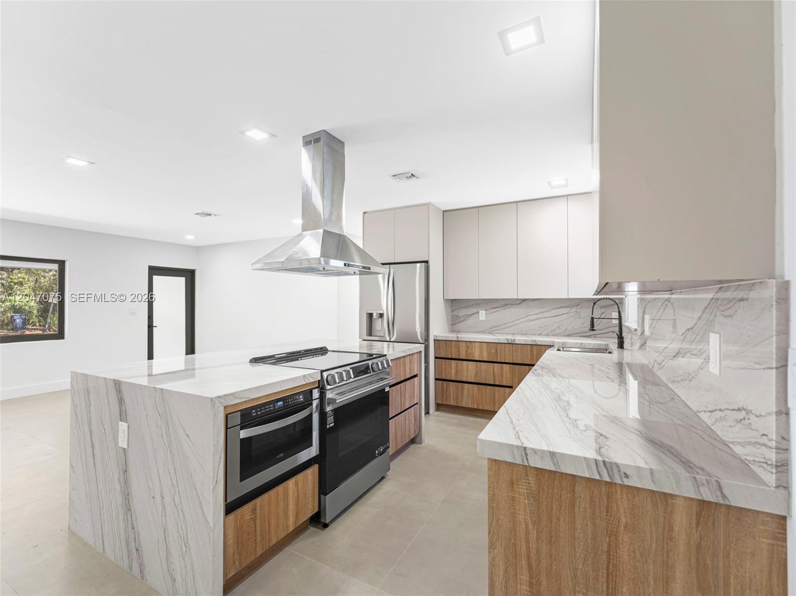 A modern kitchen features a marble-topped island, wood-grain cabinetry, and stainless steel appliances — 610 NE 164th Ter, Miami FL 33162, MIAMI, FL