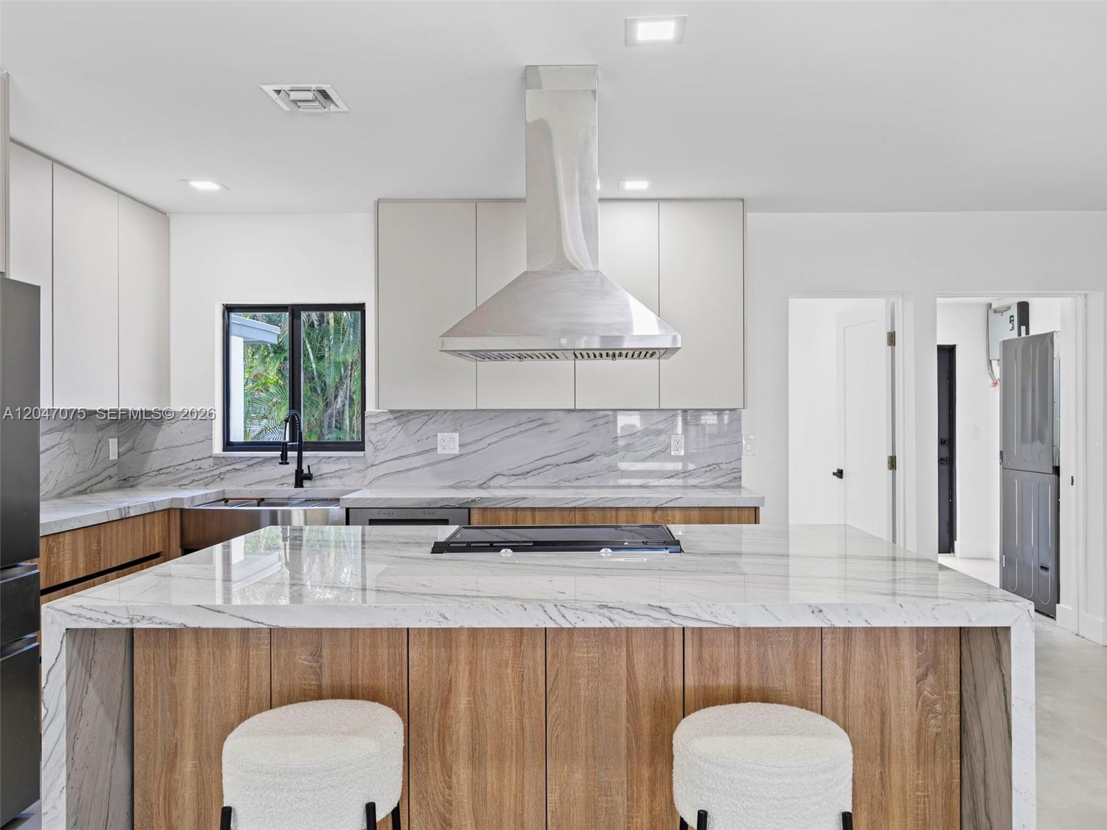 A modern kitchen features a marble-topped island, wood cabinetry, and a stainless steel range hood — 610 NE 164th Ter, Miami FL 33162, MIAMI, FL