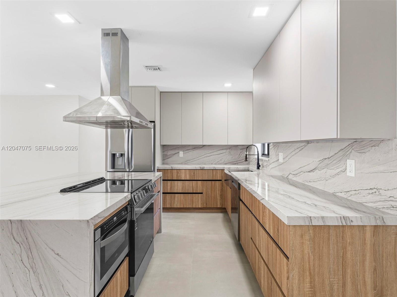 A modern kitchen features wood-grain lower cabinets, white upper cabinets, and marble countertops — 610 NE 164th Ter, Miami FL 33162, MIAMI, FL