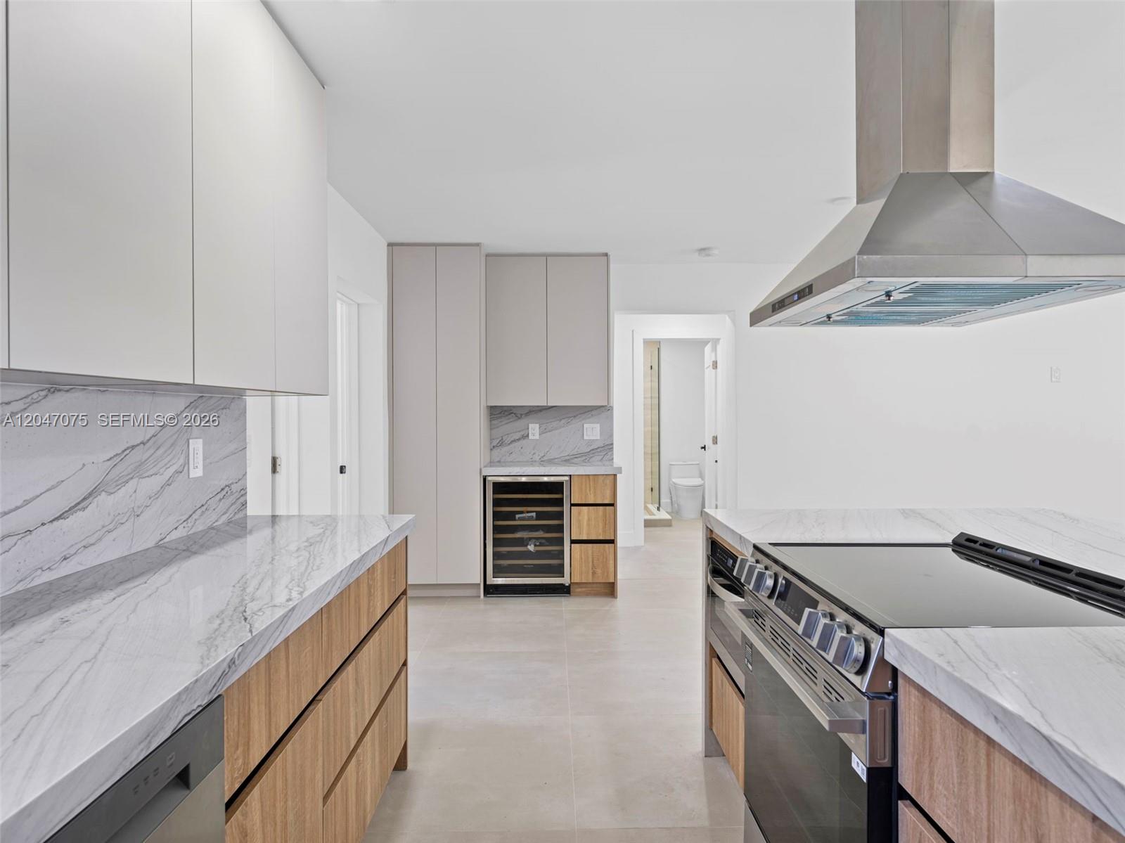 A modern kitchen features wood-toned cabinetry, marble countertops, stainless steel appliances, and a wine cooler — 610 NE 164th Ter, Miami FL 33162, MIAMI, FL