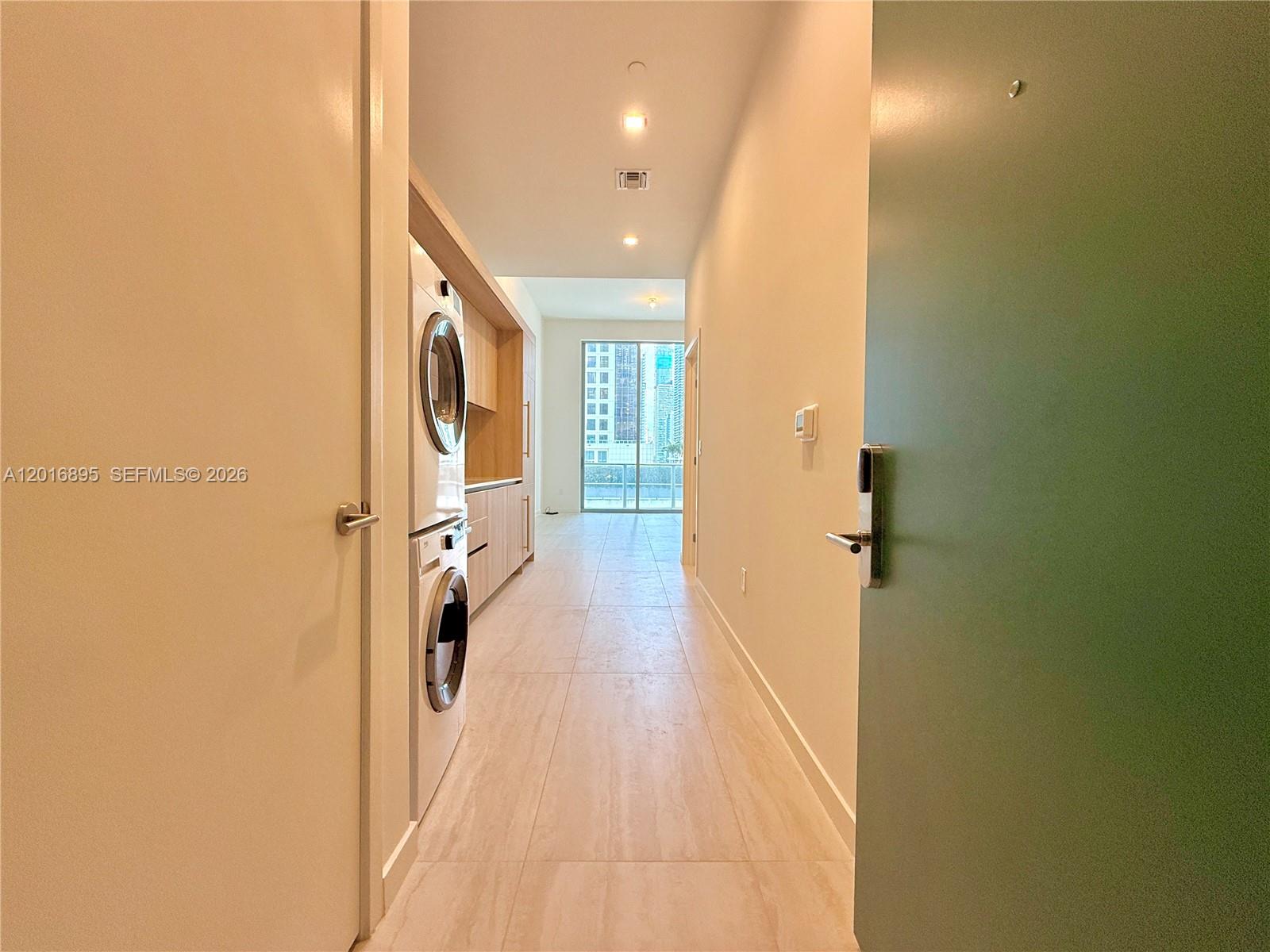 A hallway features a stacked washer and dryer, light tile flooring, and a distant window — 77 SE 5 st # 1213, Miami FL 33131, MIAMI, FL