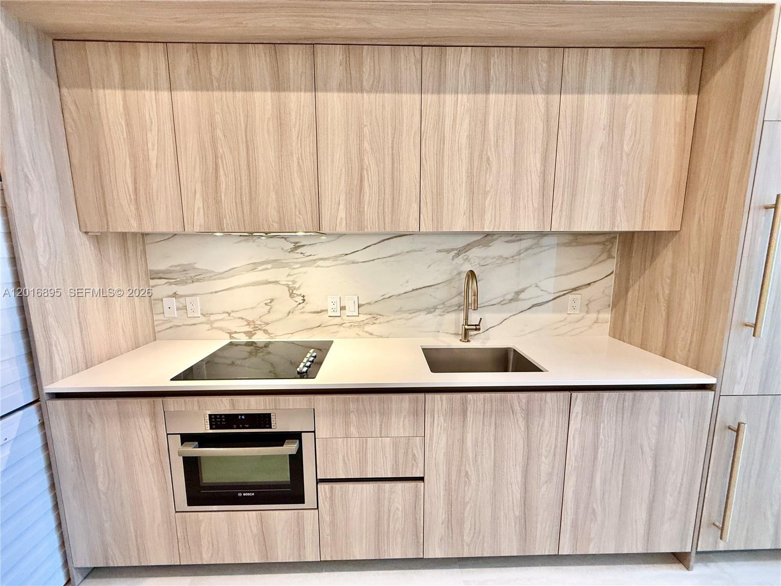 A modern kitchen features light wood cabinets, a marble backsplash, and stainless steel appliances — 77 SE 5 st # 1213, Miami FL 33131, MIAMI, FL
