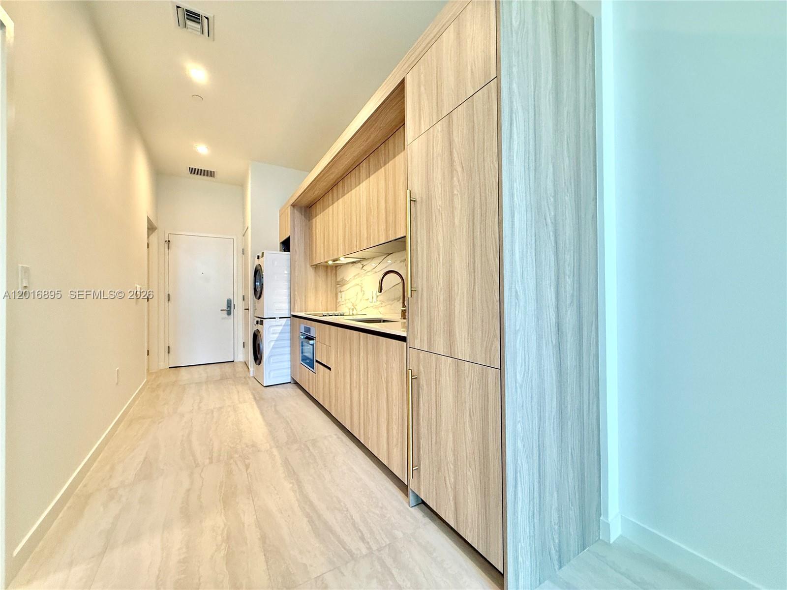 A modern galley kitchen features light wood cabinetry, stone countertops, and a stacked laundry unit — 77 SE 5 st # 1213, Miami FL 33131, MIAMI, FL