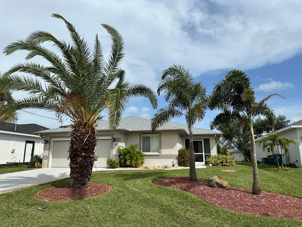 A beige house exterior features a screened front entryway, a gravel garden, and red flowering shrubs — 107 COTTAGE PLACE, ROTONDA WEST, FL