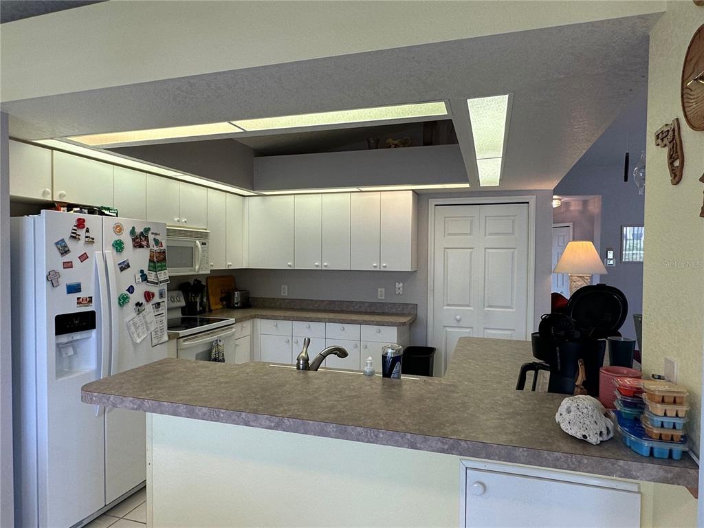 A living room with black leather recliners, a ceiling fan, and an open kitchen area — 107 COTTAGE PLACE, ROTONDA WEST, FL