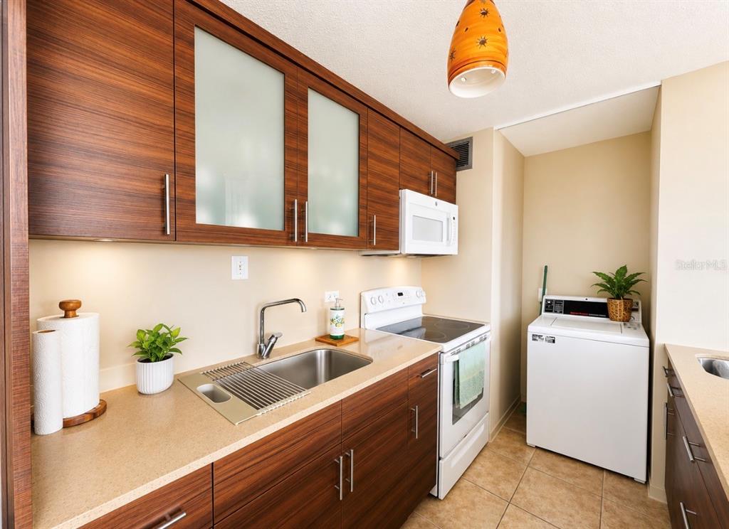 A kitchen featuring wood-grain cabinets, a stainless steel sink, white appliances, and a laundry area — Ocean Drive PLAYA AZUL UNIT 90, LUQUILLO, PR