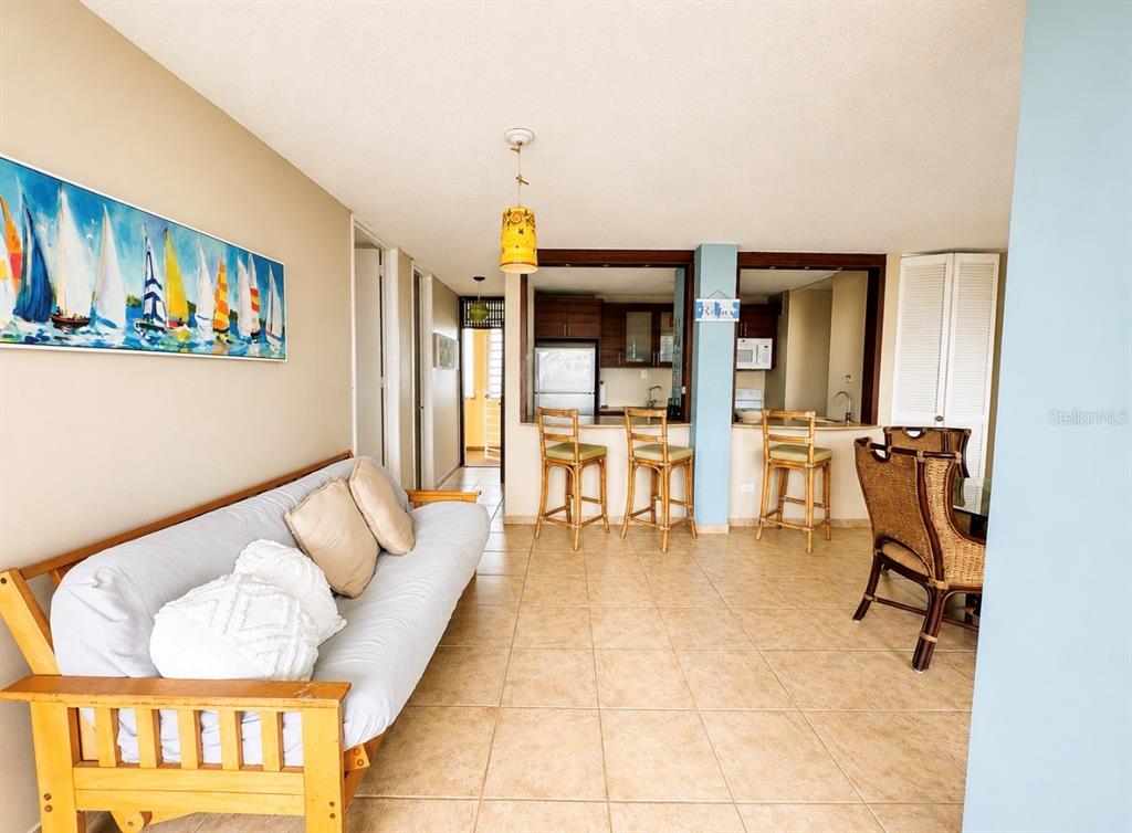 A living room with a futon, tile flooring, and a kitchen pass-through with bar stools — Ocean Drive PLAYA AZUL UNIT 90, LUQUILLO, PR