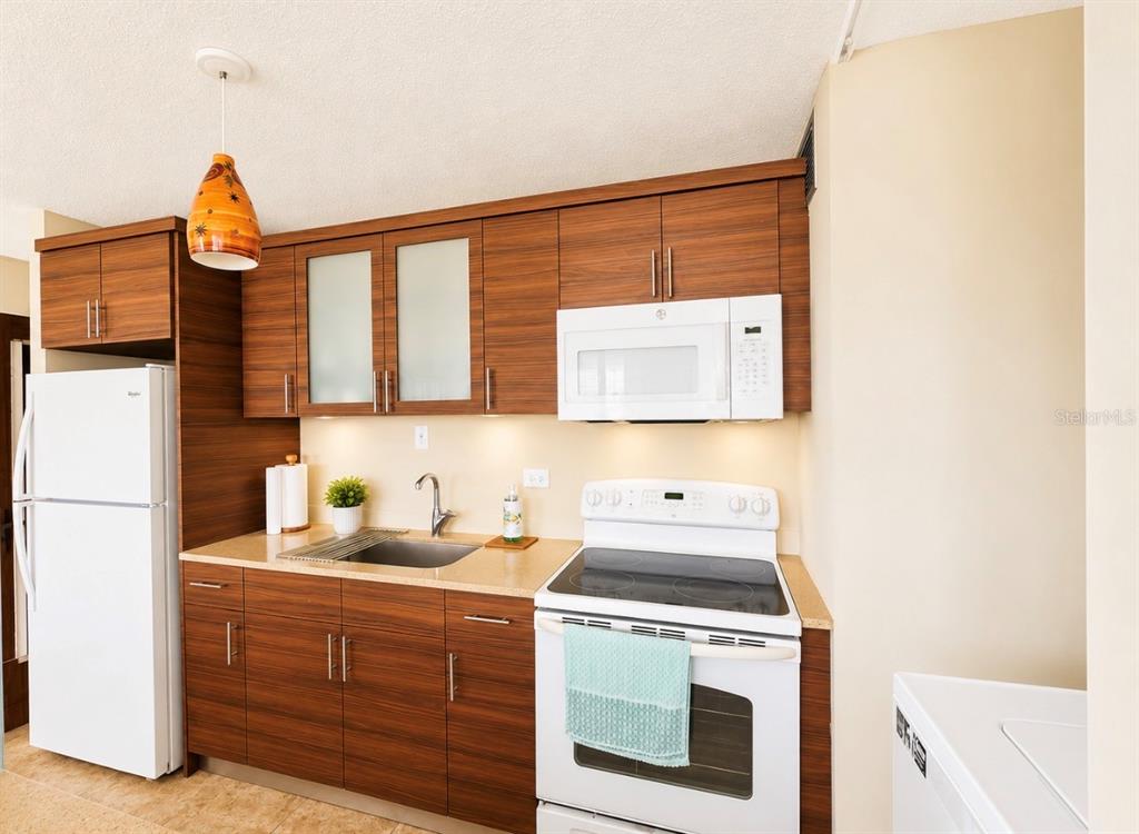 A kitchen features wood-grain cabinets, white appliances, a stainless steel sink, and a pendant light — Ocean Drive PLAYA AZUL UNIT 90, LUQUILLO, PR
