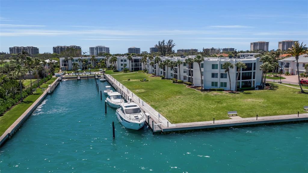 An aerial view shows a white multi-story apartment building beside a canal with docked boats — 448 GULF OF MEXICO DRIVE UNIT A205, LONGBOAT KEY, FL