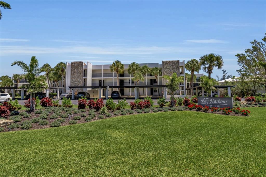 A multi-story apartment building with covered parking and a landscaped lawn in the foreground — 448 GULF OF MEXICO DRIVE UNIT A205, LONGBOAT KEY, FL