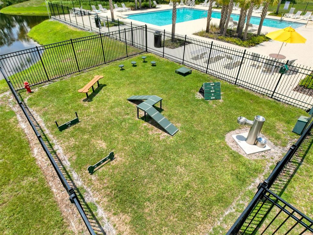 An outdoor fenced dog park features agility equipment, a water fountain, and a nearby pool — 4395 TROTTERS WAY, LAKELAND, FL