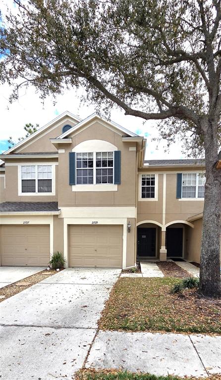 A two-story townhouse with a tan stucco exterior, two garage doors, and a large tree — 2729 CONCH HOLLOW DRIVE, BRANDON, FL