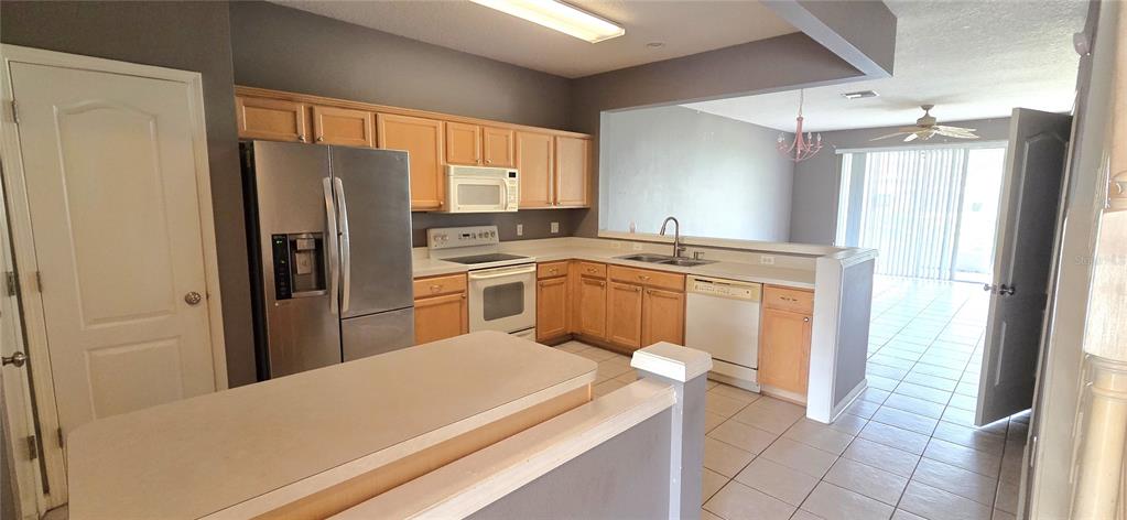 A kitchen features light wood cabinets, stainless steel appliances, and a peninsula overlooking a living area — 2729 CONCH HOLLOW DRIVE, BRANDON, FL