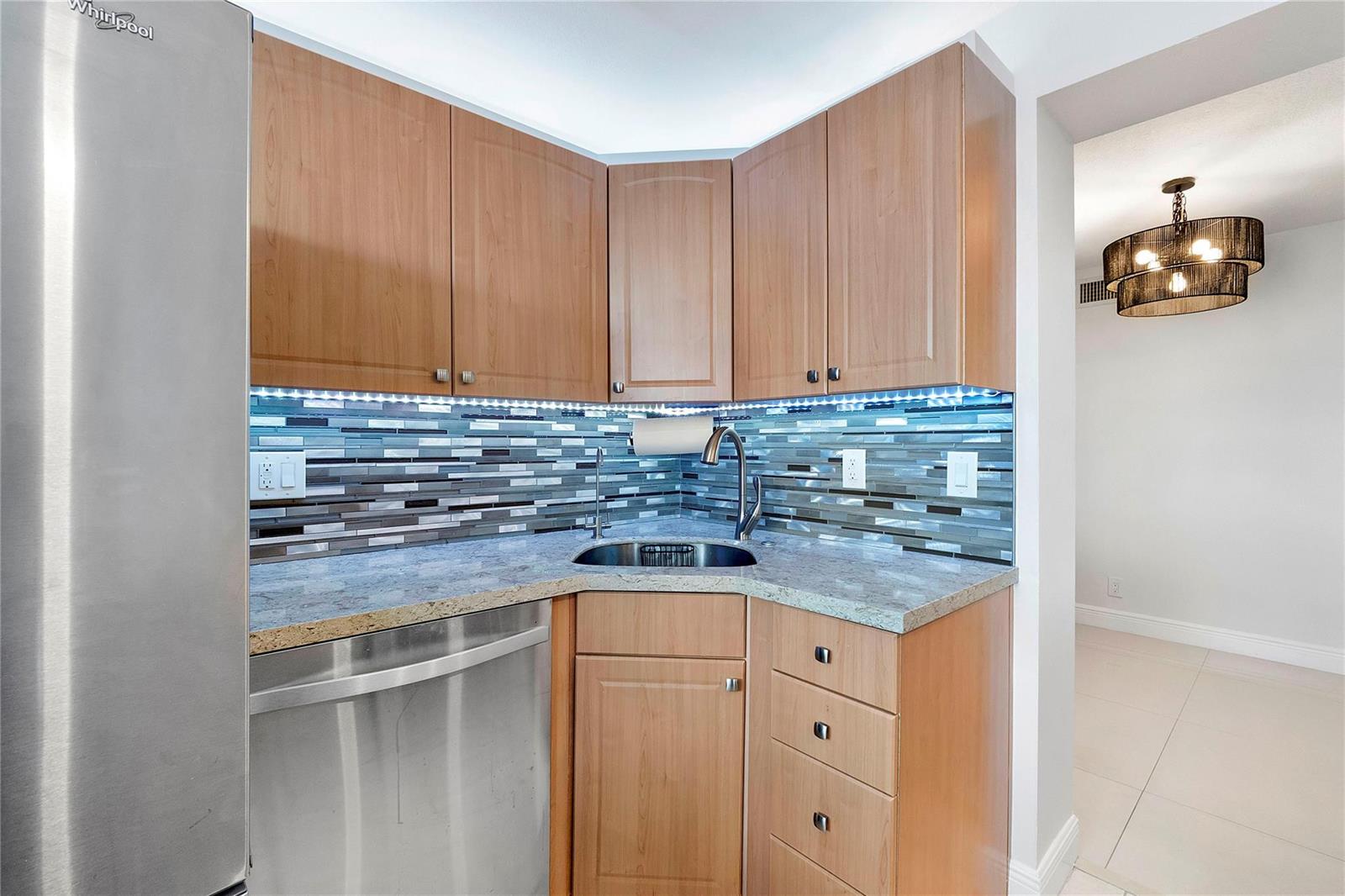 A kitchen corner features wood cabinets, a granite countertop, a stainless sink, and tiled backsplash — 1505 N Riverside Drive # 1003, Pompano Beach FL 33062, POMPANO BEACH, FL
