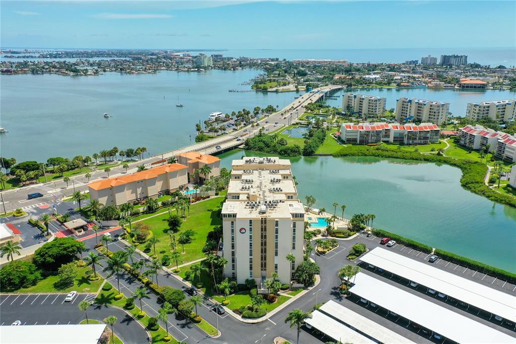 An aerial view shows a multi-story apartment building surrounded by parking, green space, and water — 7400 SUN ISLAND DRIVE UNIT 503, SOUTH PASADENA, FL