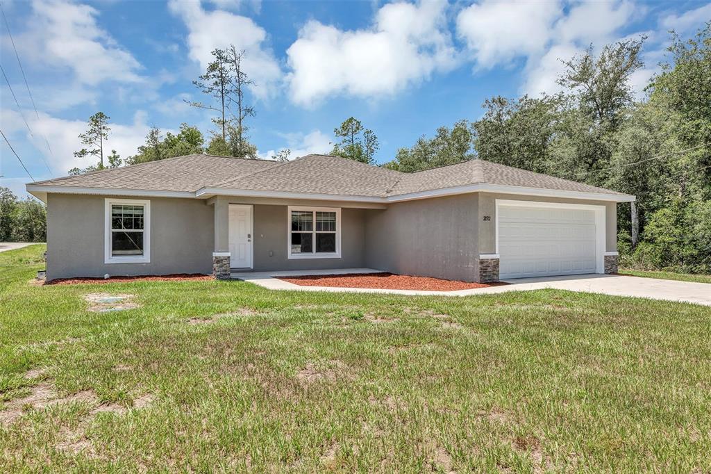 A single-story house with a gray stucco exterior, a two-car garage, and a shingled roof — 21512 SW RAINBOW LAKES BOULEVARD, DUNNELLON, FL