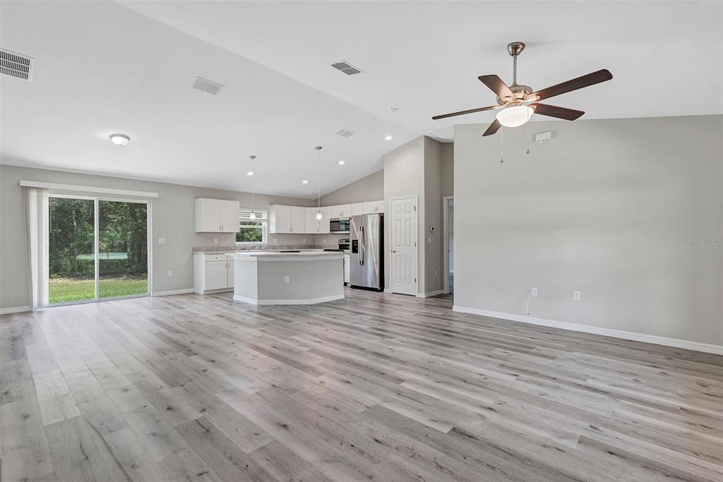 An open-concept living area features light wood-look flooring, a kitchen with white cabinets, and stainless-steel appliances — 21512 SW RAINBOW LAKES BOULEVARD, DUNNELLON, FL
