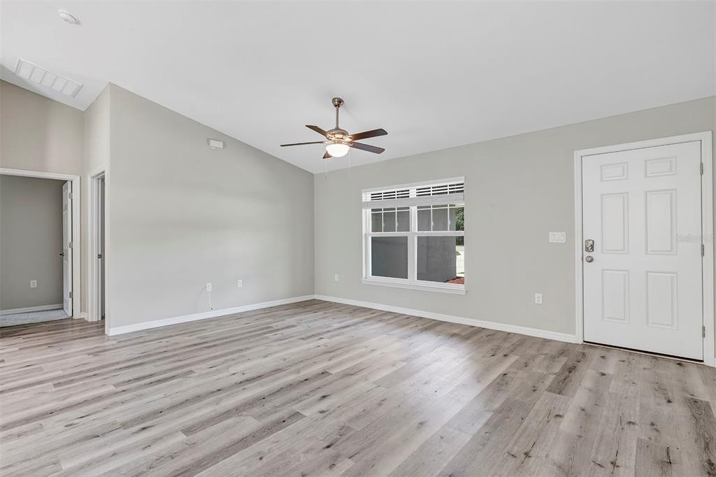 An empty living room with light gray walls, wood-look flooring, a ceiling fan, and a door — 21512 SW RAINBOW LAKES BOULEVARD, DUNNELLON, FL