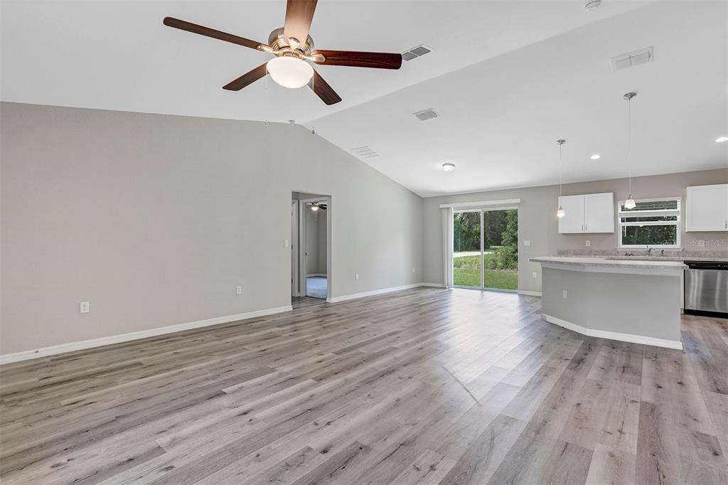 An open-concept living room and kitchen featuring vaulted ceilings, light wood-look flooring, and sliding doors — 21512 SW RAINBOW LAKES BOULEVARD, DUNNELLON, FL
