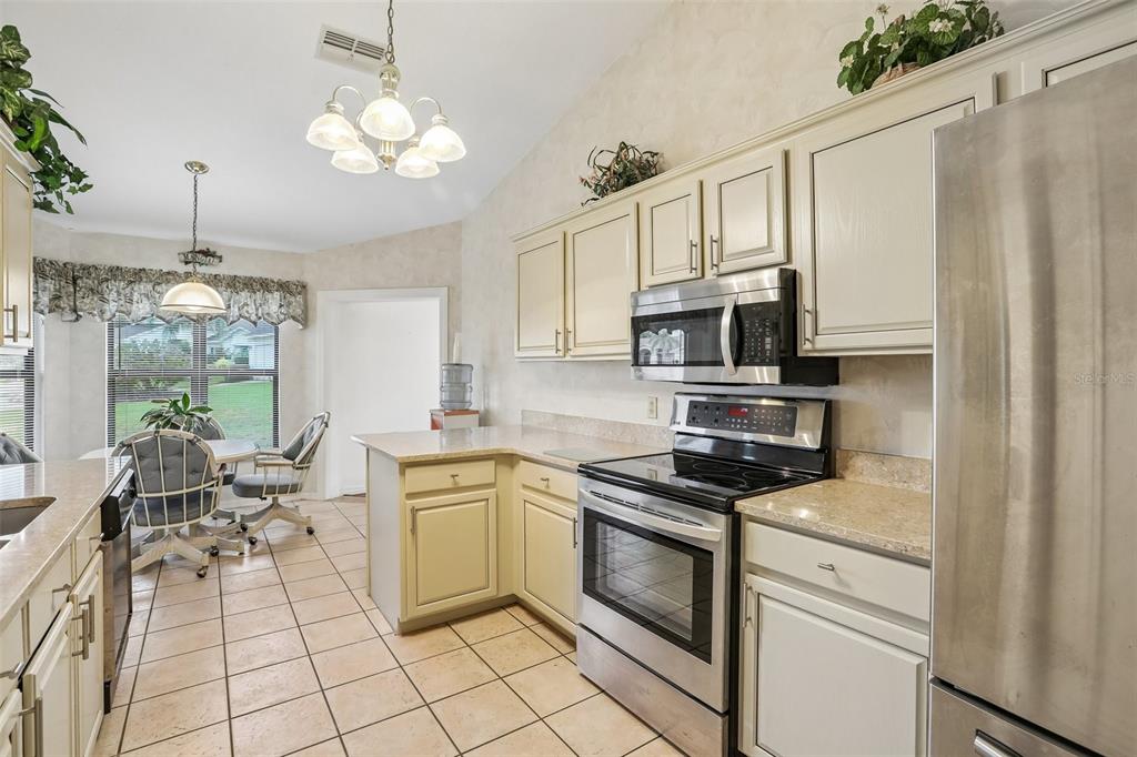A kitchen with light-colored cabinets, stainless steel appliances, tile flooring, and an adjacent dining area — 8328 PAVILION DRIVE, HUDSON, FL