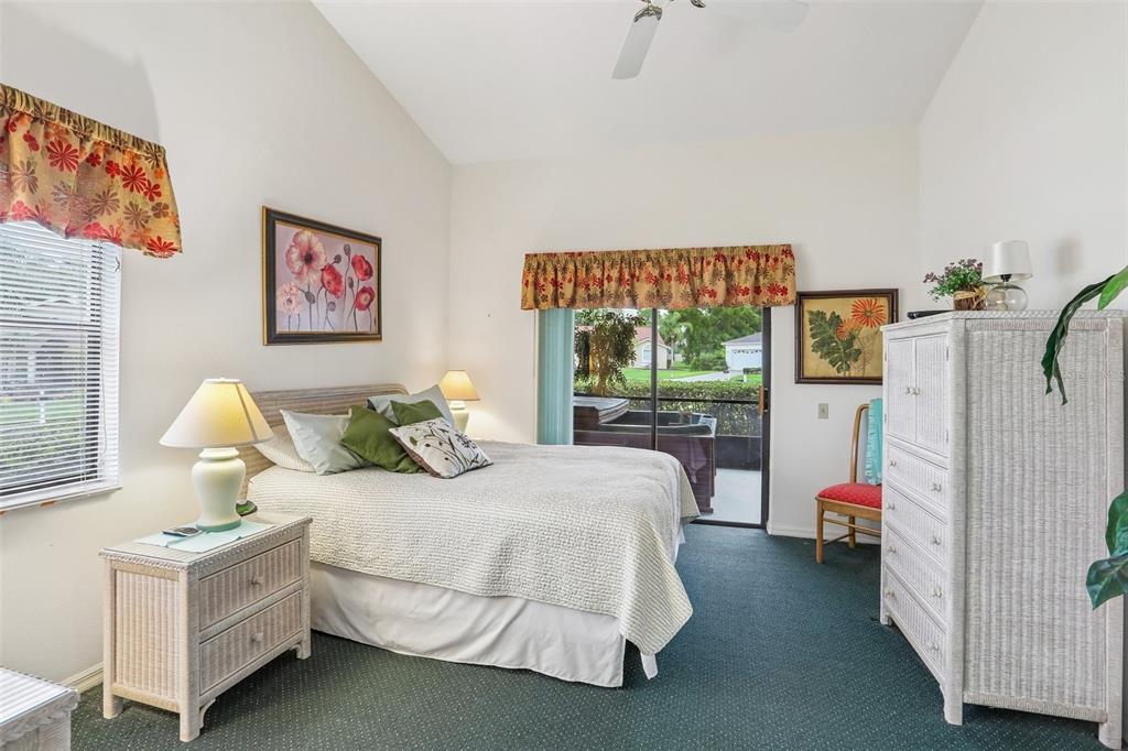 A bedroom features a bed, wicker furniture, green carpet, and a sliding glass door — 8328 PAVILION DRIVE, HUDSON, FL