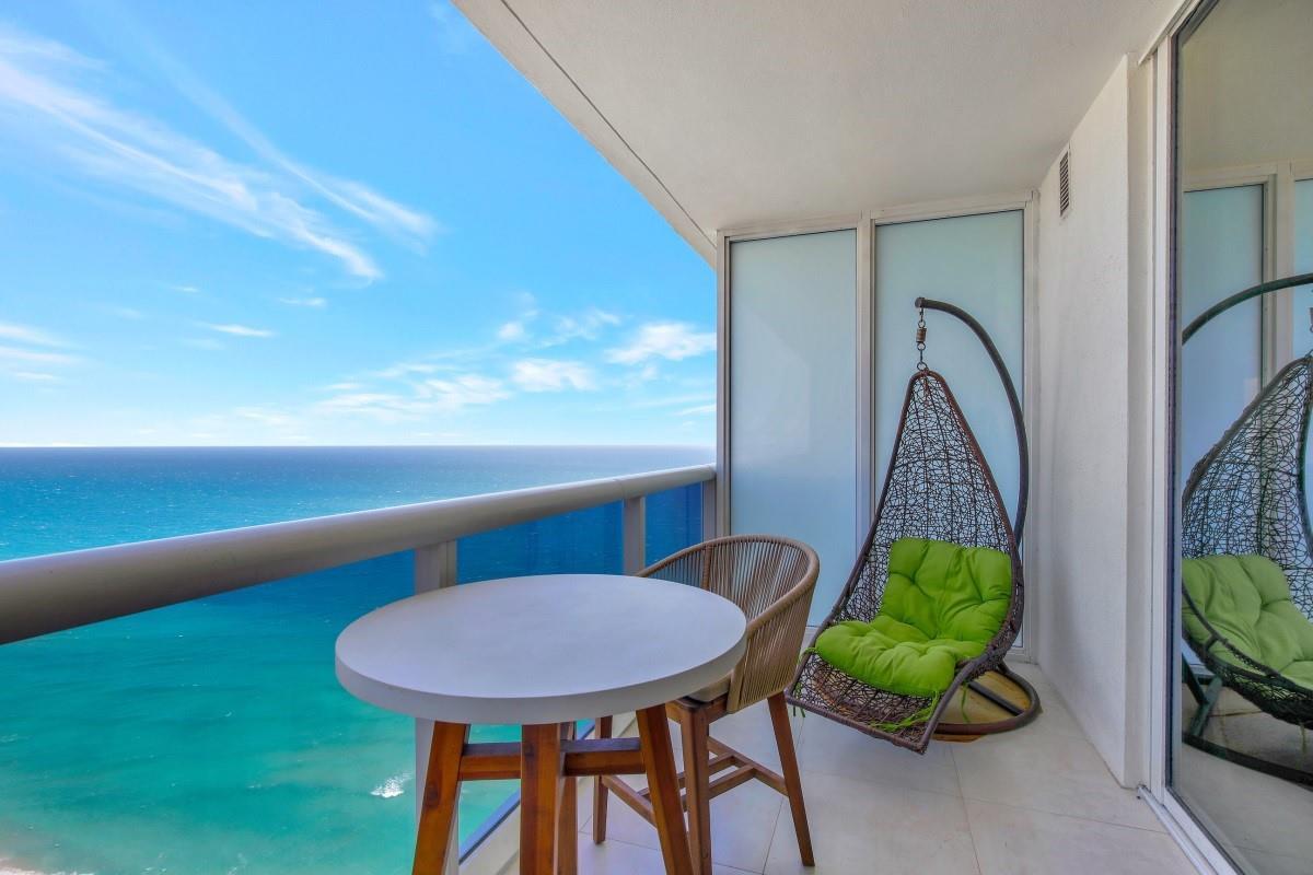 A balcony with a small table, a chair, and a hanging swing chair overlooking the ocean — 1830 S Ocean Boulevard # 4612, Hallandale Beach FL 33009, HALLANDALE BEACH, FL