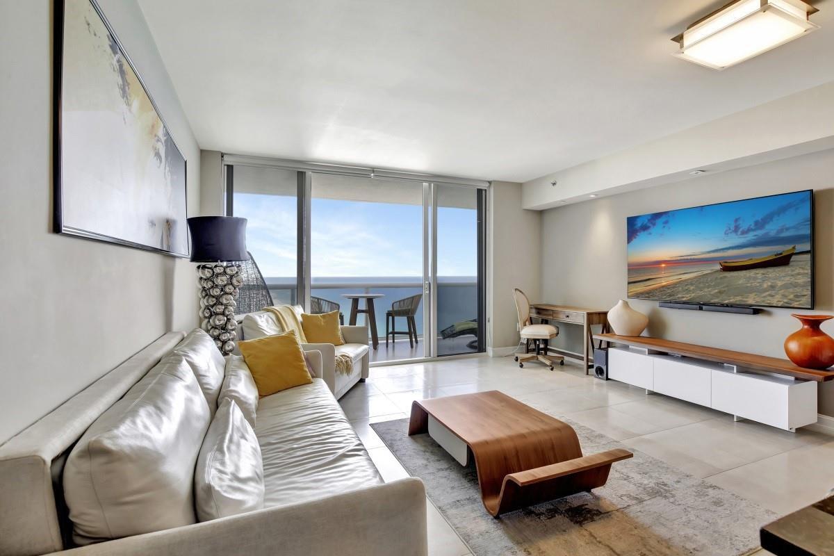 A modern living room features a white sofa, wood coffee table, and balcony with ocean views — 1830 S Ocean Boulevard # 4612, Hallandale Beach FL 33009, HALLANDALE BEACH, FL