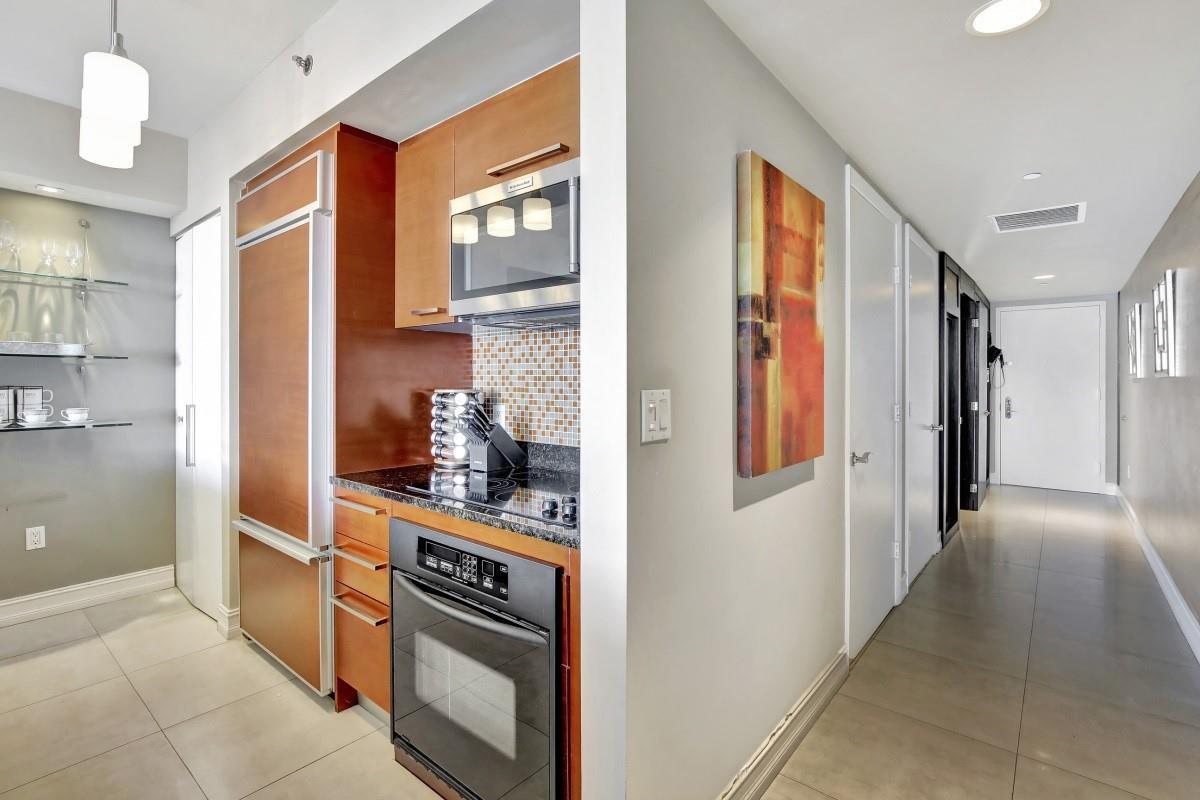 A compact kitchen with wood cabinetry and stainless steel appliances sits beside a hallway — 1830 S Ocean Boulevard # 4612, Hallandale Beach FL 33009, HALLANDALE BEACH, FL