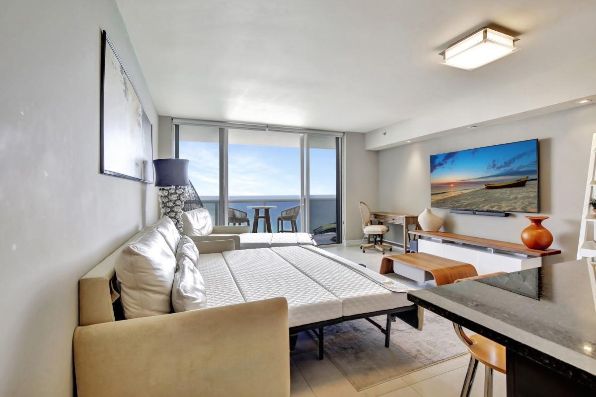 A living room features a pull-out sofa bed, a television, and a balcony with ocean views — 1830 S Ocean Boulevard # 4612, Hallandale Beach FL 33009, HALLANDALE BEACH, FL