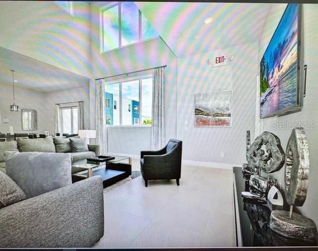 A modern living room features high ceilings, large windows, a gray sofa, and wall art — 7770 SANDY RIDGE DRIVE UNIT 207, REUNION, FL
