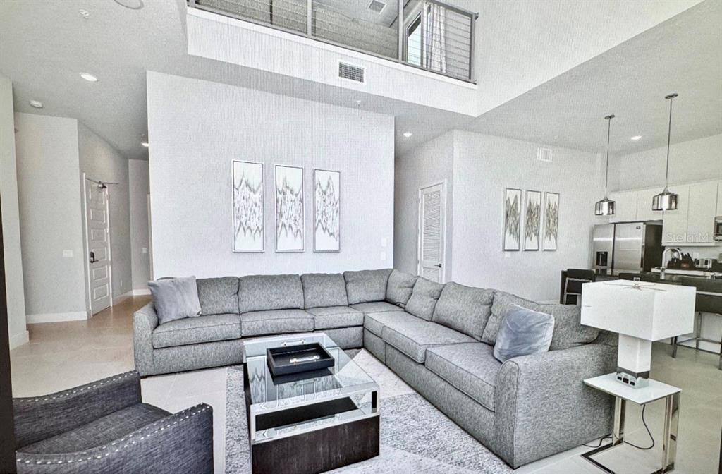 A living room features a large gray sectional sofa, a glass coffee table, and high ceilings — 7770 SANDY RIDGE DRIVE UNIT 207, REUNION, FL