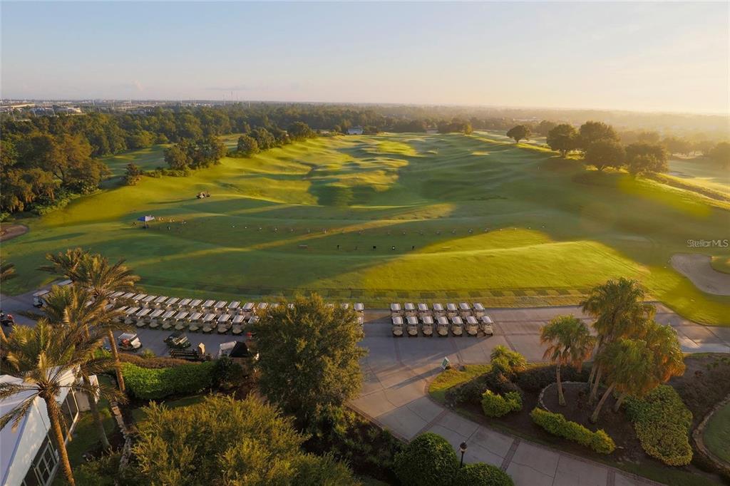 An aerial view of a golf course driving range with parked golf carts at sunrise — 7770 SANDY RIDGE DRIVE UNIT 207, REUNION, FL