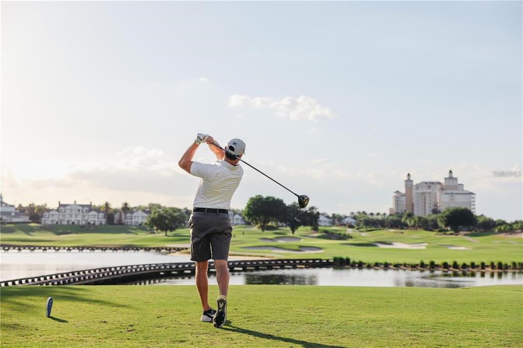 A golfer swings a club on a green course with a lake and buildings nearby — 7770 SANDY RIDGE DRIVE UNIT 207, REUNION, FL