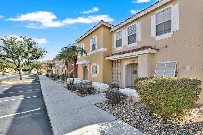 A row of multi-story townhomes with tan stucco exteriors and a paved walkway — 1070 PARK RIDGE CIRCLE, KISSIMMEE, FL