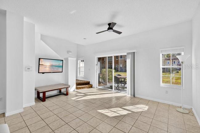A bright living room features light-colored tile flooring, a ceiling fan, and a wall-mounted television — 1070 PARK RIDGE CIRCLE, KISSIMMEE, FL