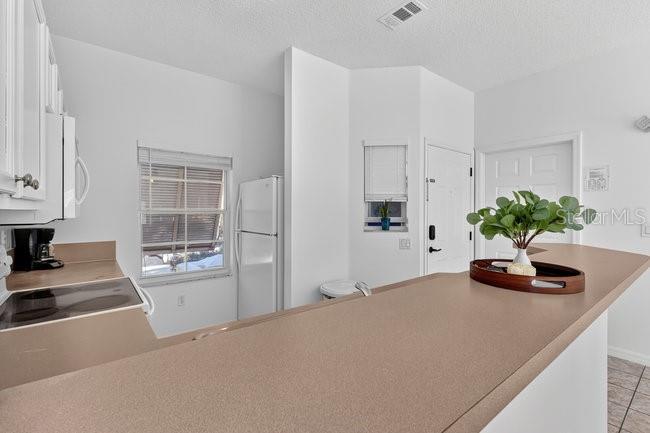 A kitchen features white cabinets, a tan countertop, a white refrigerator, and a window — 1070 PARK RIDGE CIRCLE, KISSIMMEE, FL
