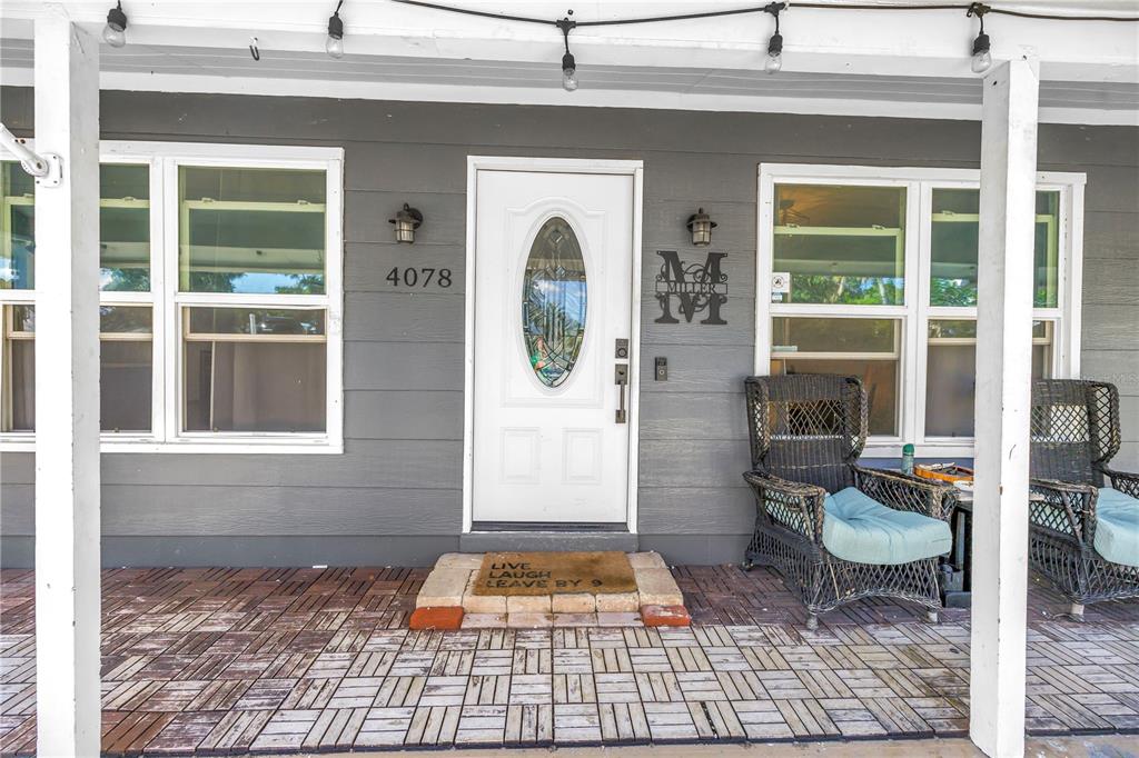 A covered front porch features gray horizontal siding, a white front door, and wicker chairs — 4078 GROVELAND AVENUE, SARASOTA, FL