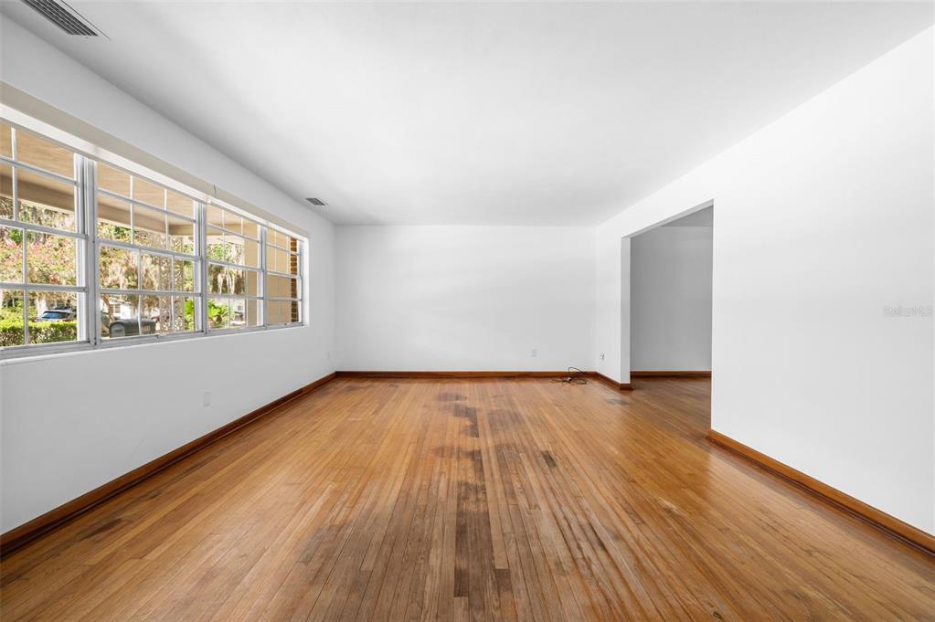 An empty room with hardwood floors, white walls, and large windows overlooking a yard — 3716 SW 6TH PLACE, GAINESVILLE, FL
